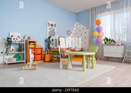 Interno della moderna sala giochi dell'asilo con scaffali, cassettiera e tavolo con sedie Foto Stock