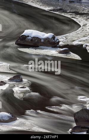 Stati Uniti, Wyoming, parco nazionale di Yellowstone. Un'esposizione prolungata crea linee di acqua sfocate che scorrono intorno alla roccia e al ghiaccio in un Lamar R parzialmente congelato Foto Stock