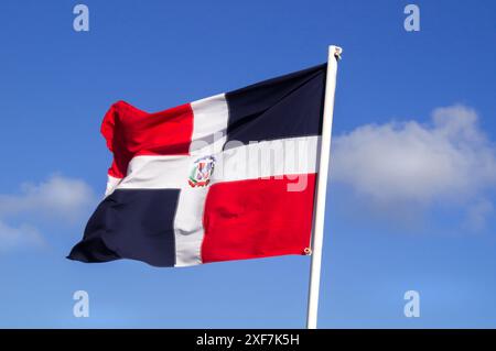 Bandiera rossa e blu della Repubblica Dominicana che sfocia contro il giglio blu con nuvola bianca. La Repubblica Dominicana è un paese dell'isola di Hispaniola Foto Stock