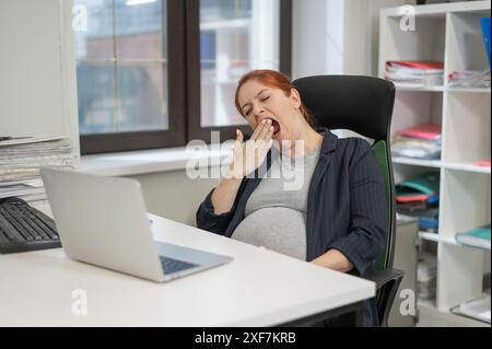 Donna incinta che dorme alla sua scrivania in ufficio. Foto Stock