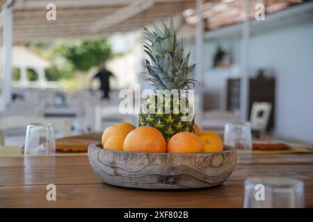 Frutta, arance e ananas in un recipiente di legno sul tavolo Foto Stock