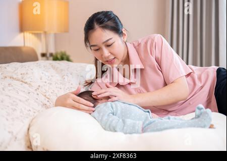 Una bella e premurosa giovane mamma asiatica sta confortando e mettendo il suo bambino appena nato a dormire in camera da letto. amore e tenerezza, maternità, genitorialità Foto Stock