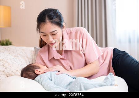 Una bella e premurosa giovane mamma asiatica sta confortando e mettendo il suo bambino appena nato a dormire in camera da letto. amore e tenerezza, maternità, genitorialità Foto Stock