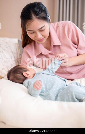 Una bella e premurosa giovane mamma asiatica sta confortando e mettendo il suo bambino appena nato a dormire in camera da letto. amore e tenerezza, maternità, genitorialità Foto Stock