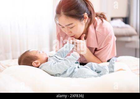 Una mamma asiatica bacia la mano del suo neonato mentre lo conforta e lo mette a dormire. legame familiare, amore e tenerezza, genitorialità, toge Foto Stock