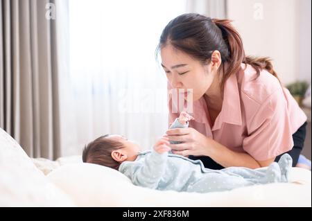 Una giovane e premurosa mamma asiatica che mette il suo bambino a dormire in camera da letto. legame familiare, amore e tenerezza, genitorialità, unione Foto Stock