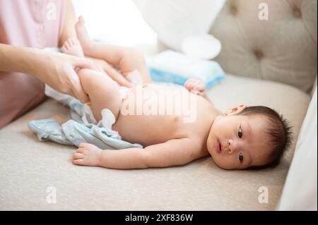 Una mamma premurosa sta cambiando i vestiti e il pannolino del suo neonato, o indossando un pannolino e un pigiama per lui sul divano del soggiorno. assistenza all'infanzia Foto Stock