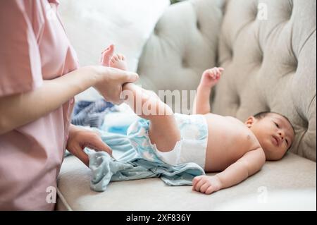 Una mamma premurosa sta cambiando i vestiti e il pannolino del suo neonato, o indossando un pannolino e un pigiama per lui sul divano del soggiorno. assistenza all'infanzia Foto Stock