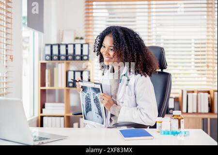 Una dottoressa nera professionale e sicura di sé con un abito bianco sta avendo un consulto online con la sua paziente, mostrando la radiografia al paziente, al wor Foto Stock