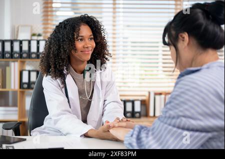 Un medico donna di colore che tiene la mano di un paziente per confortarlo e rassicurarlo durante una visita medica nella sala esame dell'hospit Foto Stock