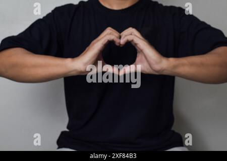 Vista di Man Hand Make Heart shape gesture per il giorno della gentilezza mondiale o san valentino con un po' sfocato Foto Stock