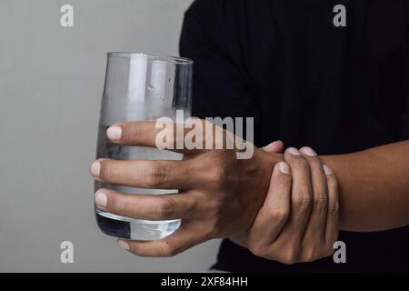 Vista di uomo tenere a portata di mano per alleviare il sintomo tremolante mentre bere acqua per il morbo di parkinson e la malattia cronica Foto Stock