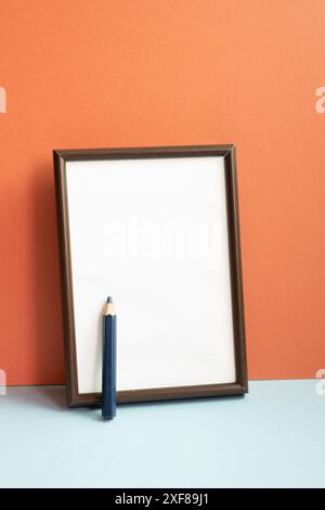 Cornice fotografica vuota con matita colorata su ripiano grigio. sfondo rosso della parete Foto Stock