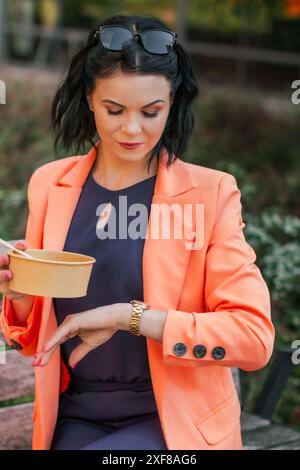 Donna d'affari che mangia un pranzo sano fuori dall'ufficio in un parco cittadino, stile di vita sano. Il pranzo è una deliziosa insalata e un pasto dietetico. Foto Stock