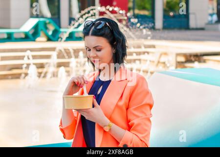 Donna d'affari che mangia un pranzo sano fuori dall'ufficio in un parco cittadino, stile di vita sano. Il pranzo è una deliziosa insalata e un pasto dietetico. Foto Stock