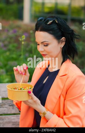 Donna d'affari che mangia un pranzo sano fuori dall'ufficio in un parco cittadino, stile di vita sano. Il pranzo è una deliziosa insalata e un pasto dietetico. Foto Stock