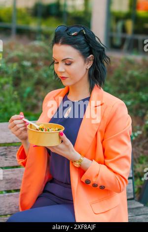 Donna d'affari che mangia un pranzo sano fuori dall'ufficio in un parco cittadino, stile di vita sano. Il pranzo è una deliziosa insalata e un pasto dietetico. Foto Stock