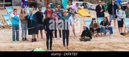 Un'immagine panoramica di persone in piedi e che guardano una gara di surf al GT Western Beach di Newquay in Cornovaglia nel Regno Unito. Foto Stock