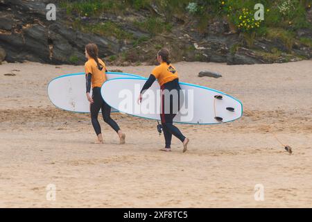 Due surfisti principianti portano le loro tavole da surf e camminano fuori dal mare dopo una lezione di surf al GT Western Great Western Beach di Newquay a Cornwal Foto Stock