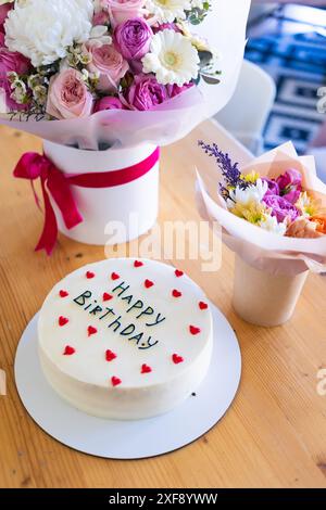 Torta di compleanno con le parole Happy Birthday scritte sopra, circondata da decorazioni a cuore rosso. Foto Stock