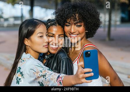 Amiche che condividono un gioioso momento di selfie in un ambiente urbano al crepuscolo. Foto Stock