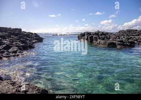 Bellissima spiaggia di lava durante il giorno. Le rocce laviche si alternano a acque cristalline. Paesaggio costiero con una barriera corallina e dolci onde di un'isola in Foto Stock