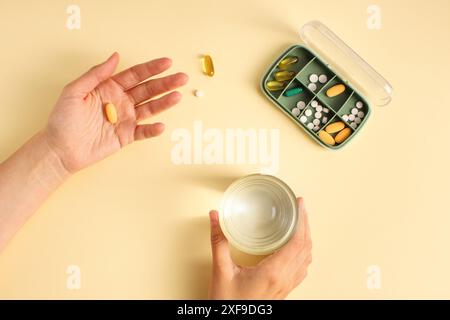 Donna che tiene un bicchiere d'acqua e pillole, c'è una scatola di pillole nelle vicinanze, vista dall'alto Foto Stock