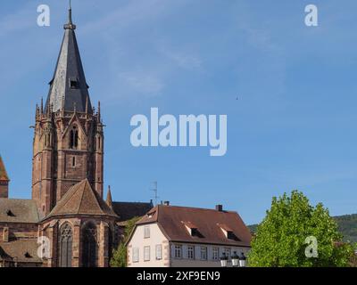 Torre della Chiesa con tetto a punta di fronte al cielo blu e agli edifici vicini, wissembourg, francia Foto Stock