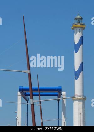 Un faro alto con strisce bianche e blu e alberi di barca in primo piano contro un cielo azzurro, ostenda, belgio Foto Stock