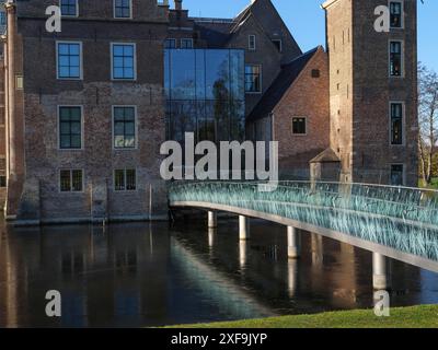 Primo piano di un castello con facciata in vetro, ponte moderno e edificio storico in mattoni, riflesso nell'acqua, a ruurlo, a gheldria, nei paesi bassi Foto Stock
