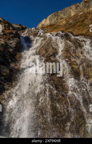 Un'impressionante cascata che scende lungo pendii rocciosi in un paesaggio montano soleggiato, saas Fee, svizzera Foto Stock