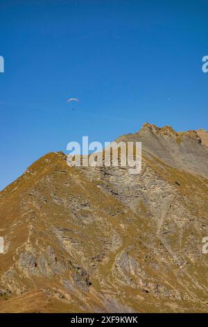 Parapendio che sorvola un paesaggio roccioso di montagna sotto un cielo blu, saas Fee, graubuenden, svizzera Foto Stock