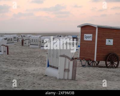 Diverse sedie a sdraio e un rimorchio sulla spiaggia al tramonto, Spiekeroog, mare del nord, germania Foto Stock