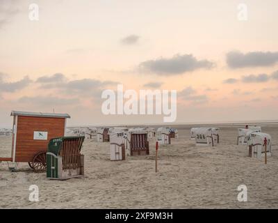 Ampia spiaggia di sabbia con sdraio e cielo nuvoloso al tramonto, crepuscolo chiaro, Spiekeroog, mare del nord, germania Foto Stock