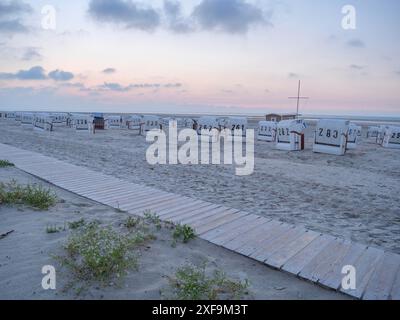 Sedie a sdraio sparse sulla spiaggia con un sentiero in legno in primo piano al tramonto, Spiekeroog, mare del nord, germania Foto Stock