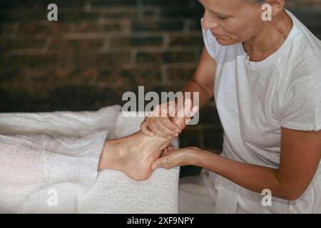 Massaggiatrice che applica olio per massaggi a piedi mentre fa un massaggio rilassante ai piedi Foto Stock