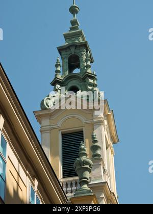 Torre della chiesa barocca con elementi decorativi di fronte a un cielo blu brillante, Vienna, Austria Foto Stock