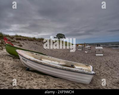 Due barche distese su una spiaggia sabbiosa sotto un cielo nuvoloso, con sedie da spiaggia vuote sullo sfondo, Zingst, Mar baltico, germania Foto Stock