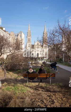 Gente sulle panchine del Jardin Truillot, in una bella giornata di sole, a Parigi, in Francia. La chiesa di Saint-Ambroise è sullo sfondo. Foto Stock