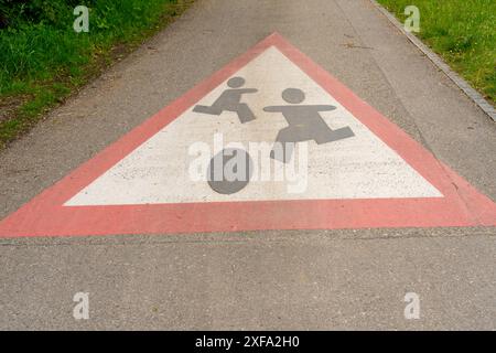 Cartello di avvertimento per bambini che giocano grande dipinto su una stradina, che conduce attraverso prati e pennelli. Foto Stock