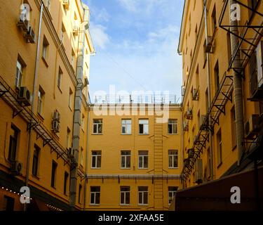 Vista dal basso di un tipico pozzo cortile nel centro storico di Mosca, Russia. Effetto tunnel. Pareti in mattoni gialli illuminate dal sole e da un frammento di cielo blu. Foto Stock