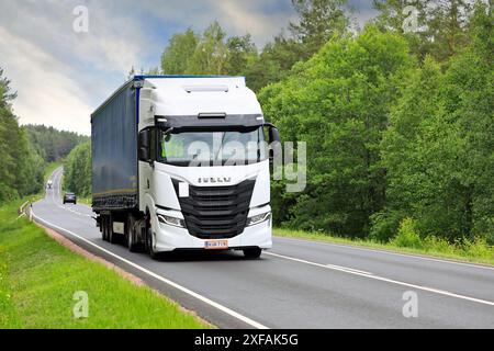 Il camion Iveco S-Way bianco tira in salita un semirimorchio a lato di un tratto curvilineo lungo l'autostrada 52 in un giorno d'estate. Salo, Finlandia. 19 giugno 2024. Foto Stock