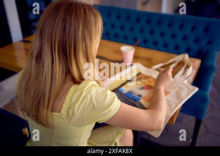 un giovane artista con un abito giallo dipinge una borsa della spesa personalizzata Foto Stock