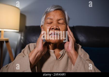 donna anziana con sintomo di perdita dell'udito seduto su un divano nel soggiorno di notte Foto Stock