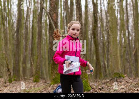 Grodno, Bielorussia - 25 marzo, 2023: Forte ragazza caucasica adolescente indossare abbigliamento sportivo che corre attraverso una foresta durante l'esercizio in esterni orienteering Gr Foto Stock