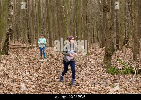 Grodno, Bielorussia - 25 marzo, 2023: Forte ragazza caucasica adolescente indossare abbigliamento sportivo che corre attraverso una foresta durante l'esercizio in esterni orienteering Gr Foto Stock