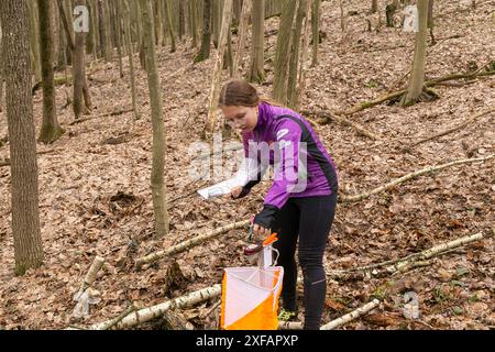 Grodno, Bielorussia - 25 marzo, 2023: Forte ragazza caucasica adolescente indossare abbigliamento sportivo che corre attraverso una foresta durante l'esercizio in esterni orienteering Gr Foto Stock