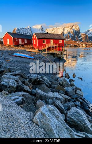 Case rosse e villaggio di fronte a montagne innevate, fiordo, alba, Reine, Moskenesoya, Lofoten, Norvegia, Europa Foto Stock