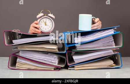 Donna stanca esausta con caffè e sveglia, una pila di cartelle di file, esaurimento, stress e sovraccarico, pressione sul lavoro Foto Stock