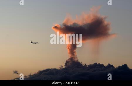 Aeroplano, jet, in avvicinamento all'aeroporto di Humberto Delgado LPPT, davanti a nuvole in una luce drammatica sotto forma di eruzione vulcanica, Lisbona, sera Foto Stock